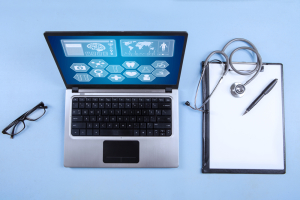 Laptop computer on table next to glasses, stethoscope, pen, and notepad